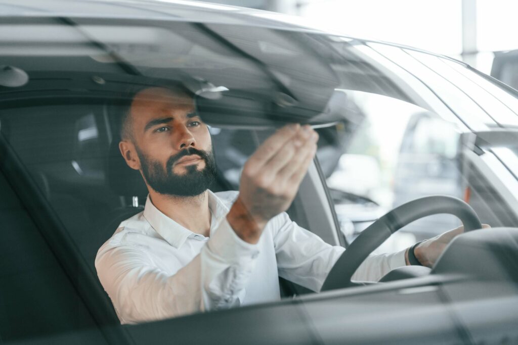 Inside of the automobile. Young man in white clothes is in the car dealership
